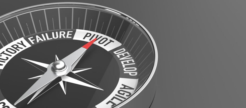 Gray and black circle compass with red needle pointing at the word pivot