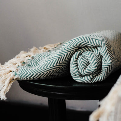 Green and white blanket with white tassels rolled up sitting on black stool