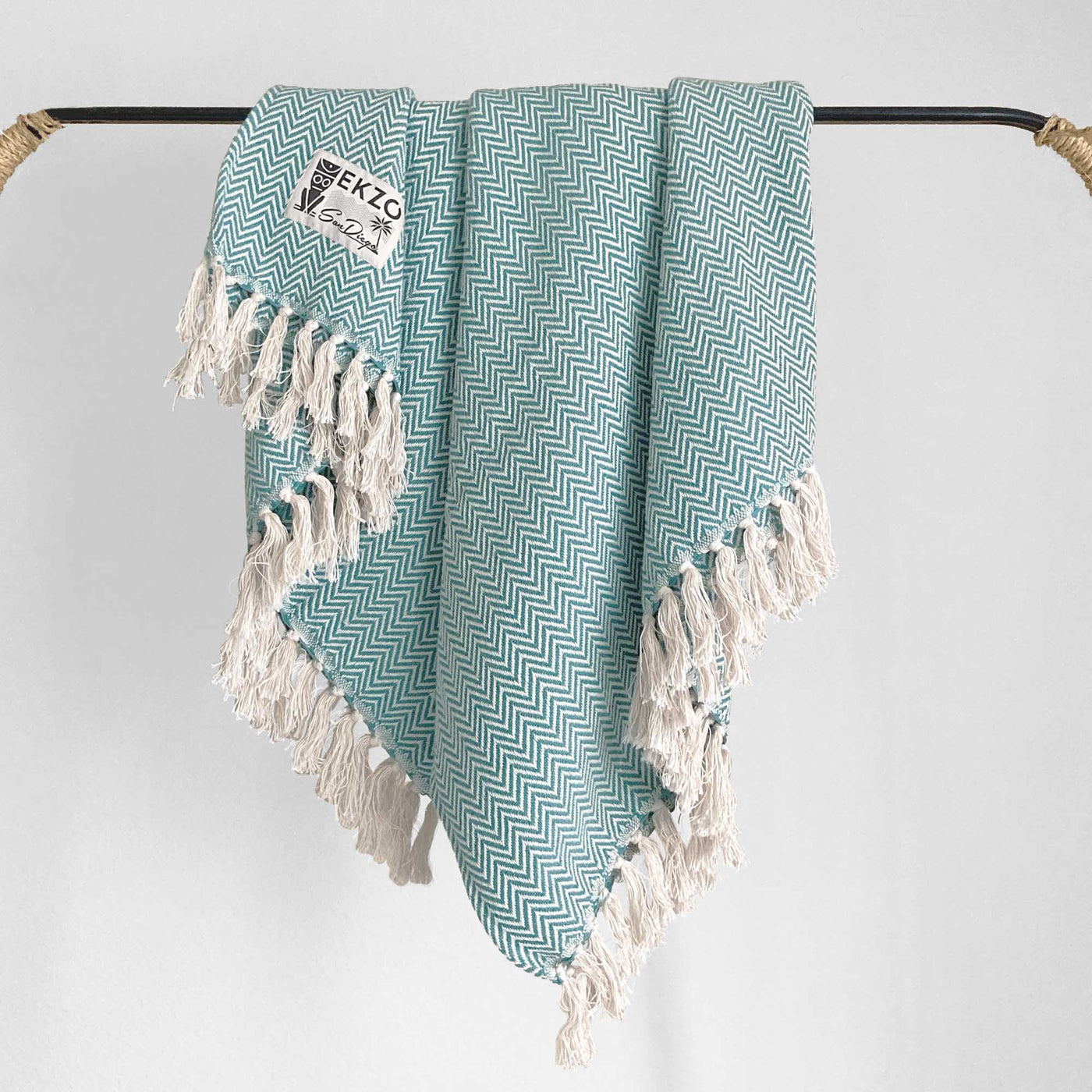 Green and white woven blanket with white tassels hanging on rack