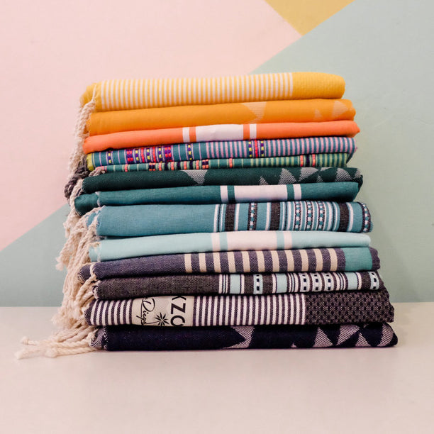 Colorful beach towels stacked in front of pink, green, and gold accent wall