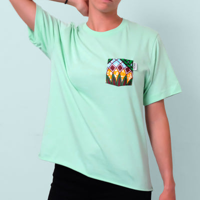 Woman posing with arm on head wearing mint green t-shirt with floral chest pocket