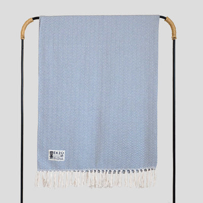 Blue and white woven blanket with white tassels hanging on rack